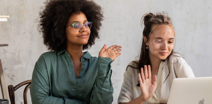 two ladies waving in front of laptop